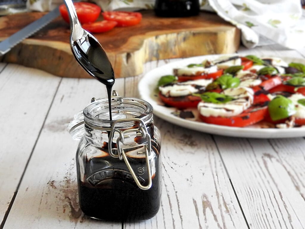 Balsamic glaze dripping off a spoon into a jar
