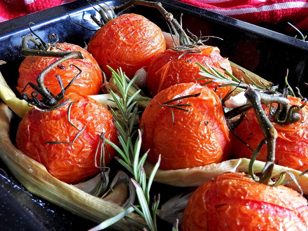 Close up of roasted leeks and tomatoes in a baking tray