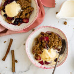 Apple and blueberry crumble in bowls with a jug of cream