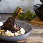 Minted lamb shank in a bowl with potato and a glass of wine