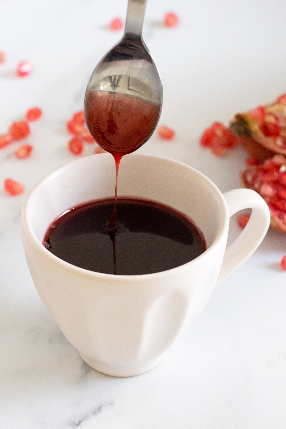 Pomegranate Molasses dripping from a spoon into a cup