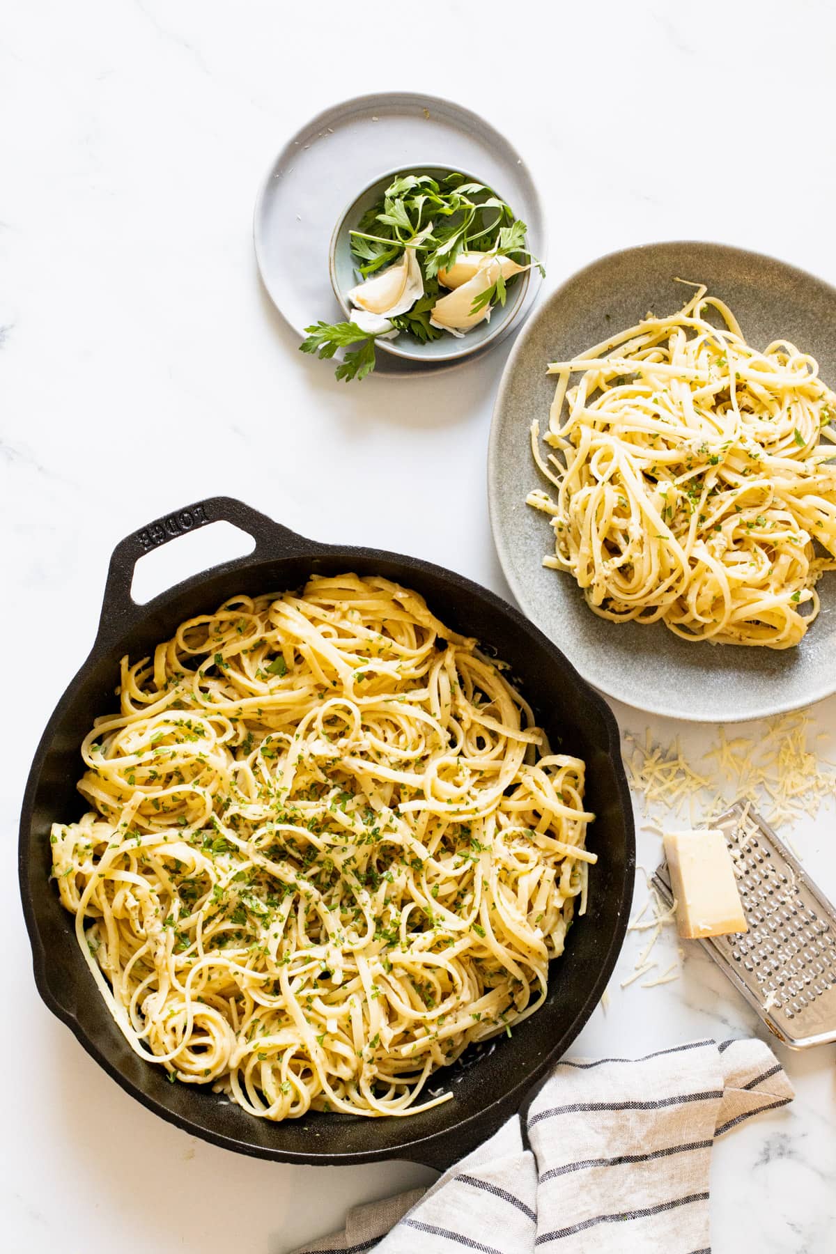 Cheesy pasta in a pan with a bowl and grated cheese