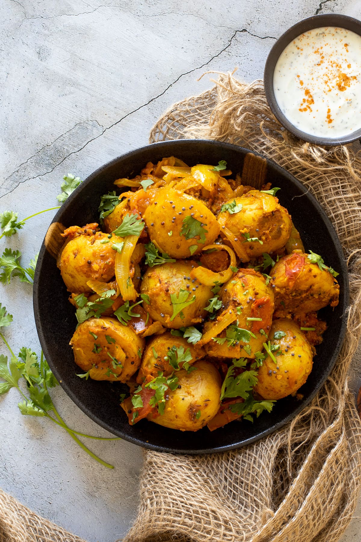 Bombay aloo in a pan with a bowl of yogurt dressing